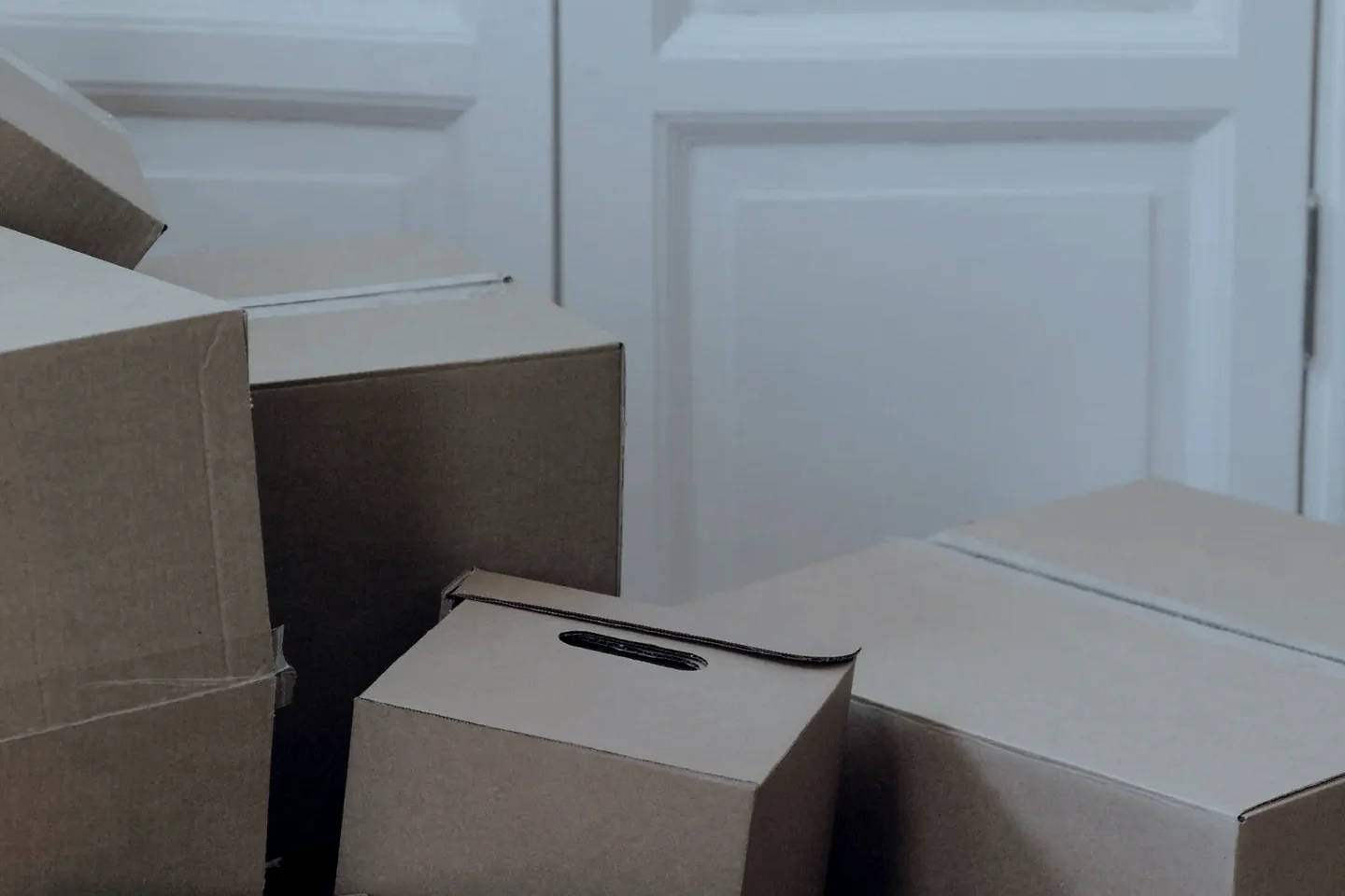 Cartons de déménagement empilés devant une porte à panneaux blancs, pièce vidée