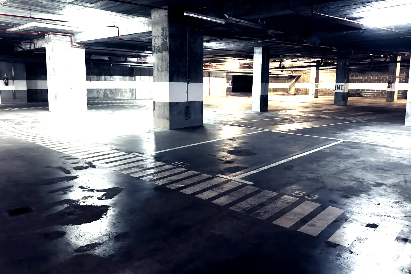 Parking souterrain vide : places marquées au sol, poteaux peints, béton humide